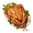 Roasted whole turkey on a platter with fresh figs and herbs, festive holiday dinner centerpiece.